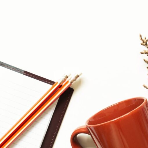 Open notebook with pencils, a terracotta mug and dried flowers on a white desk, representing a quiet space for reflection and gentle momentum.