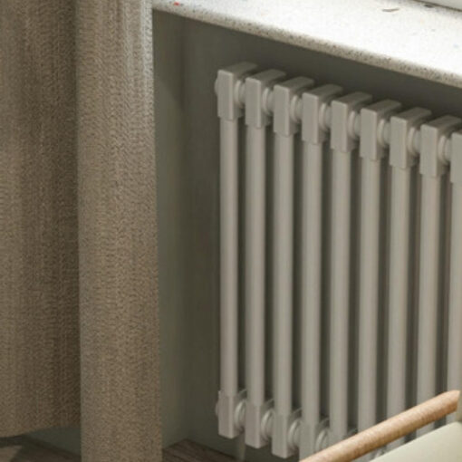 A cream column radiator beneath a window sill, with a leafy plant and a soft curtain beside it